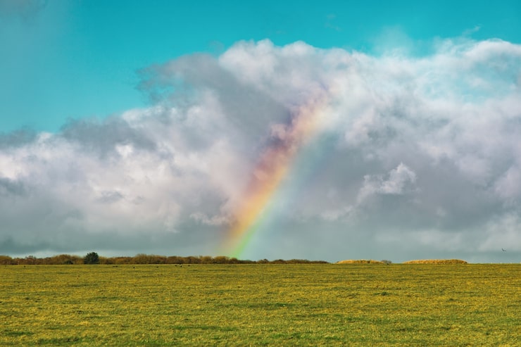 Gratis Bild vacker bild av ett tomt gräsfält med en regnbåge i fjärran under en blå molnig himmel