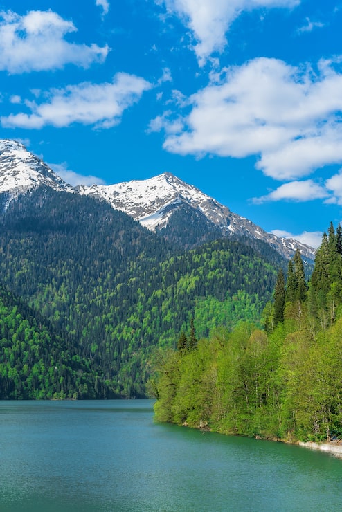 Gratis Bild vacker sjö ritsa i kaukasusbergen. gröna bergssluttningar, blå himmel med moln. vårlandskap.