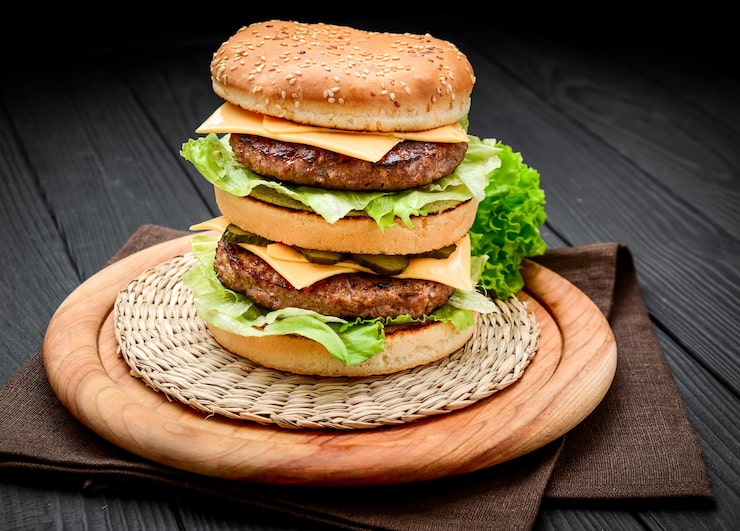 Photo một chiếc cheeseburger đôi kiểu cổ điển với hai miếng thịt bò, sốt, xà lách, phô mai, dưa chua và hành tây trên bánh mì mè