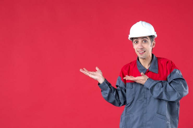 Miễn phí Photo góc nhìn từ trên xuống của một công nhân trẻ bối rối mặc đồng phục đội mũ bảo hiểm trên nền tường đỏ cô lập