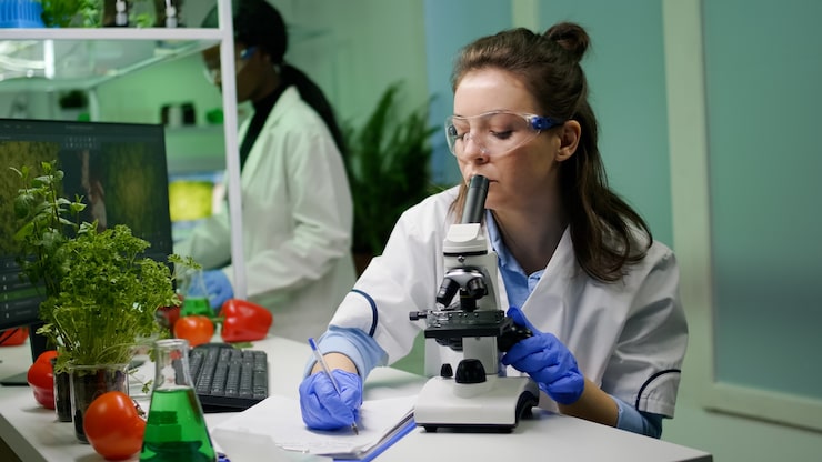Ilmainen Kuva biologi tutkija katselee lehtinäytettä lääketieteellisellä mikroskoopilla samalla kun kirjoittaa gmo-asiantuntemusta muistilehtiöön. kemisti tutkii biologista löytöä kasvista työskennellessään lääkelaboratoriossa