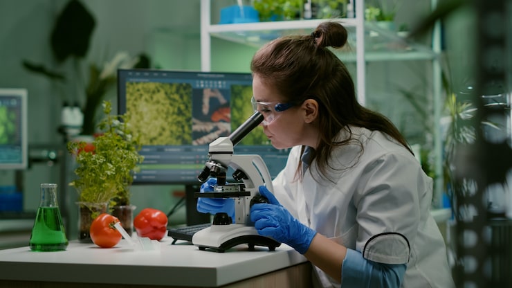 Ilmainen Kuva biologitutkijan muotokuva valkoisessa takissa työskentelemässä asiantuntijalaboratoriossa katsoen mikroskoopilla analysoiden orgaanista gmo-lehteä