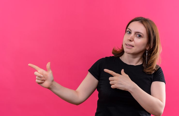 Ilmainen Kuva luottavainen nuori rento nainen osoittaa vasemmalle puolelle eristetyssä vaaleanpunaisessa tilassa