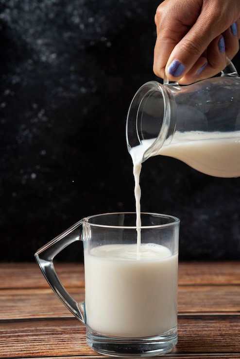 Photo gratuit femme versant du lait dans la table en bois de tasse en verre.