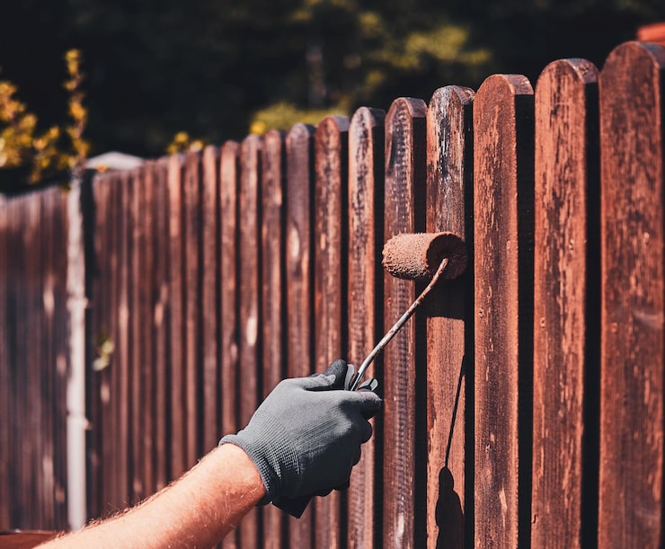 Photo gratuit un homme portant des gants de protection peint une clôture en bois par une belle journée d'été.