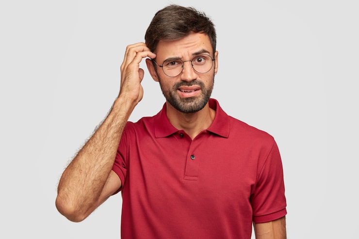 Photo gratuit intrigué jeune homme émotionnel posant contre le mur blanc