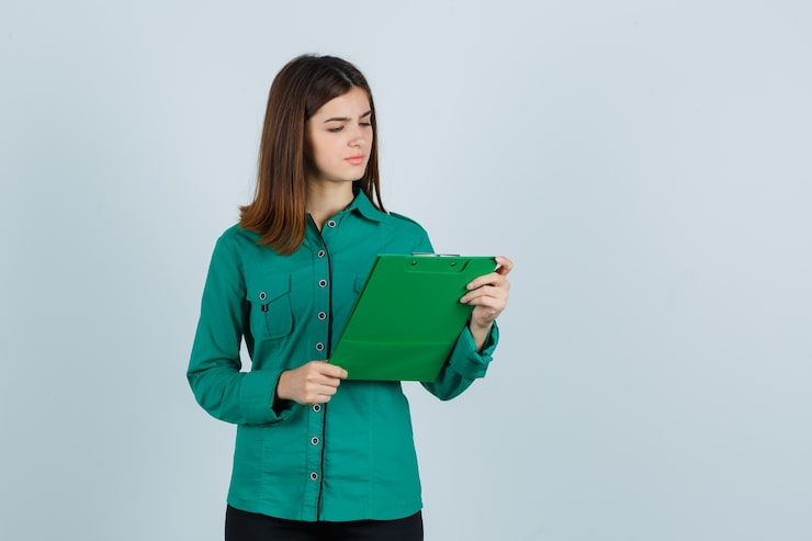Photo gratuit jeune fille regardant le presse-papiers en chemisier vert, pantalon noir et à la confusion, vue de face.