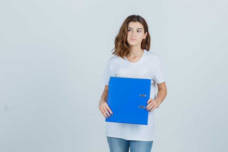 Photo gratuit jeune fille en t-shirt blanc à la recherche de suite tout en tenant le dossier et à la vue de face, focalisée.
