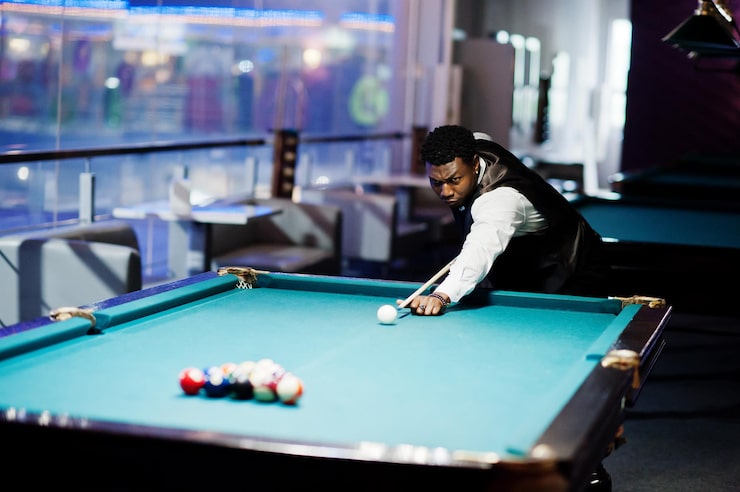 Photo gratuit un jeune homme africain beau portant une chemise blanche un gilet noir et un nœud papillon joue au billard