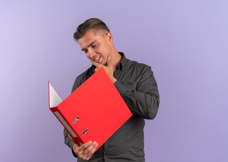 Photo gratuit jeune homme beau blond heureux tient et regarde le dossier de fichiers isolé sur l'espace violet avec copie espace