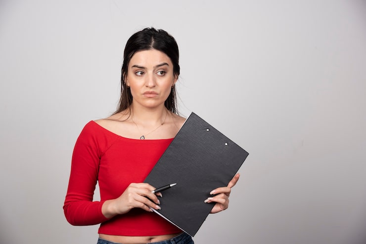 Photo gratuit jeune jolie fille en blouse rouge tenant un presse-papiers et un stylo.