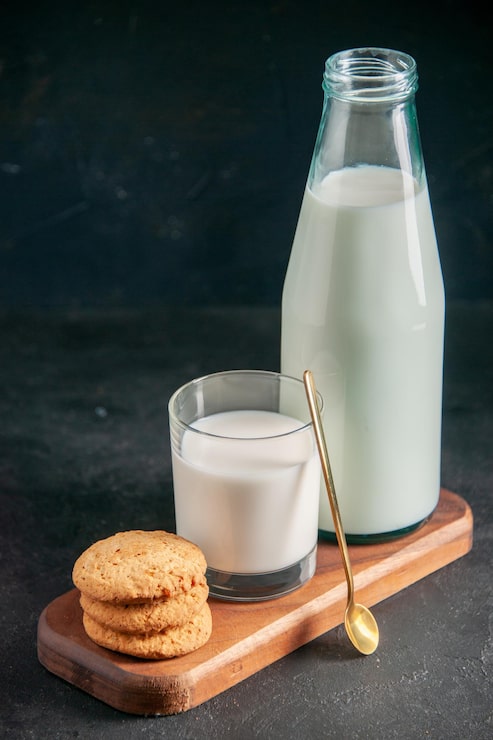 Photo gratuit vue de face d'un délicieux lait en verre et bouteille de biscuits empilés à la cuillère dorée sur un plateau en bois sur une surface sombre