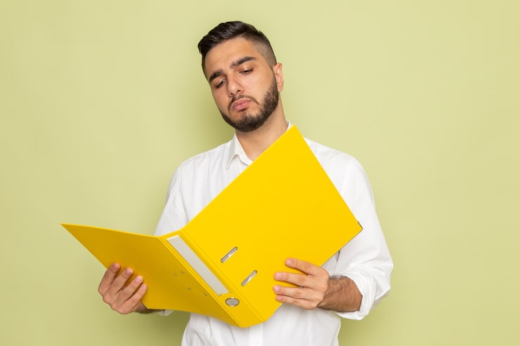 Photo gratuit une vue de face jeune homme en chemise blanche tenant des fichiers jaunes et la lecture