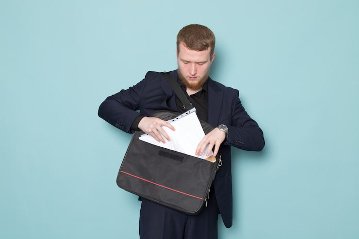 Photo gratuit une vue de face jeune mâle attrayant avec barbe en costume moderne classique noir foncé tenant des fichiers sac à dos sur l'espace bleu