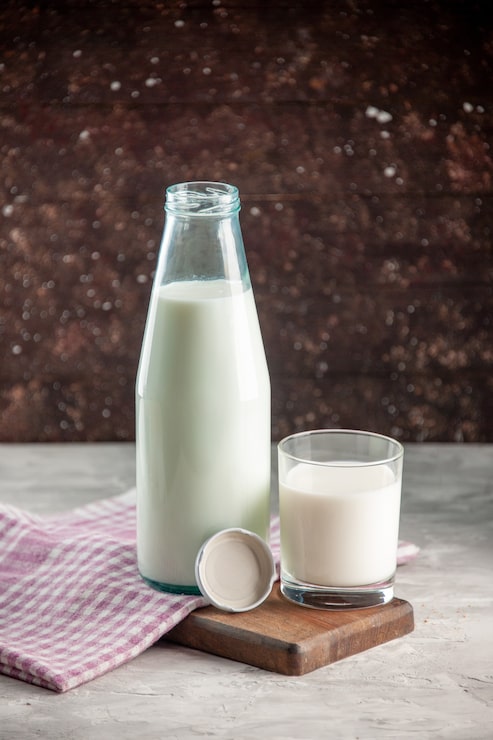 Photo gratuit vue verticale d'une bouteille en verre ouverte et d'une tasse remplie de lait sur une serviette dénudée violette sur une planche à découper en bois
