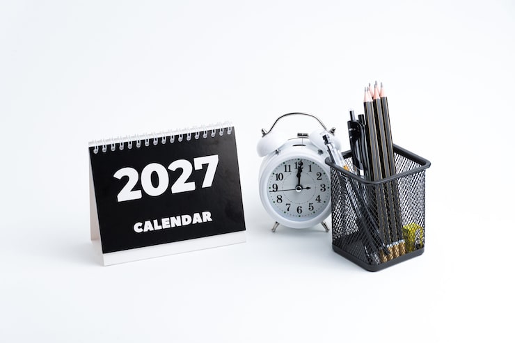 Photo aménagement de bureau avec calendrier-horloge 2027 et crayons, isolé sur blanc