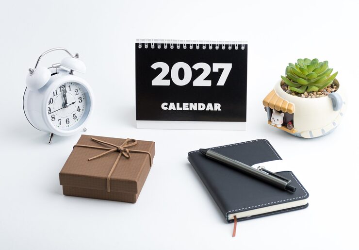 Photo aménagement de bureau pour 2027 avec calendrier, carnet, réveil et stylo sur fond blanc