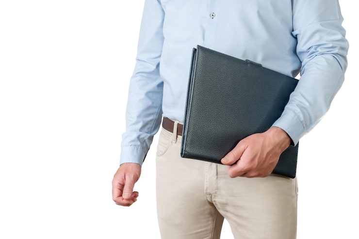 Photo homme en chemise bleu clair et pantalon beige tenant un dossier sous le bras sur fond blanc