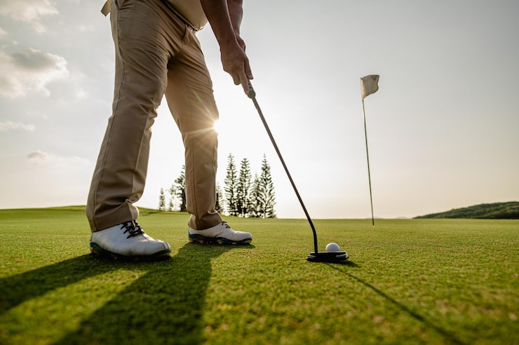 Photo homme golfeur visant une balle de golf dans une position prête à frapper un trou de golf sur l'herbe verte pendant la journée