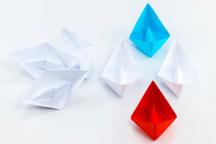 Photo navire de papier rouge et navire de papier bleu en tête parmi les navires de papier blanc