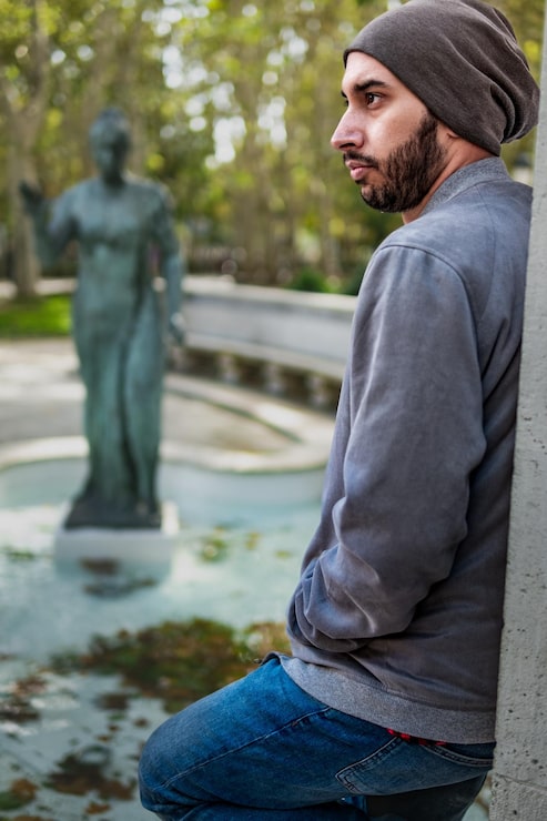 Foto læner sig op ad parkmuren i profil med en fjern statue i baggrunden