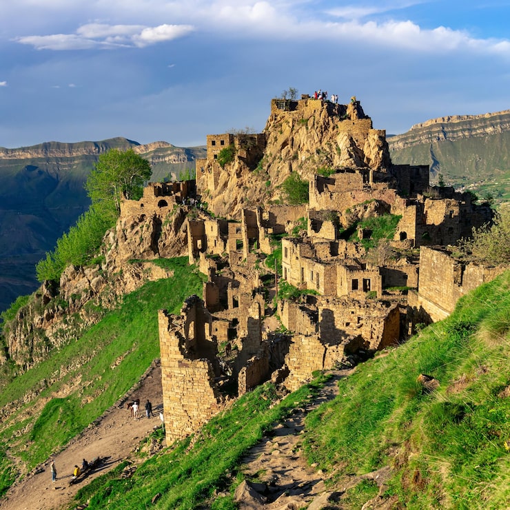 Bild utsikt över den övergivna byn gamsutl på en bergstopp i dagestan med turister bland ruinerna och på vägen nedanför