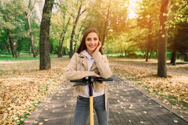 Foto jonge mooie stijlvolle vrouw rijdt op een elektrische scooter door het herfstpark ecologisch vervoer