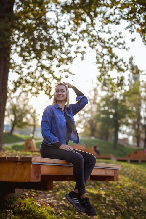 Foto modieus blond glimlachend bosnisch meisje zit op de bank in het park