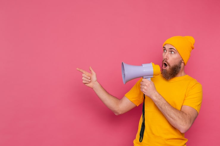Ücretsiz Fotoğraf dikkat! pembe arka planda megafonlu avrupalı adam sola doğru parmağını gösteriyor
