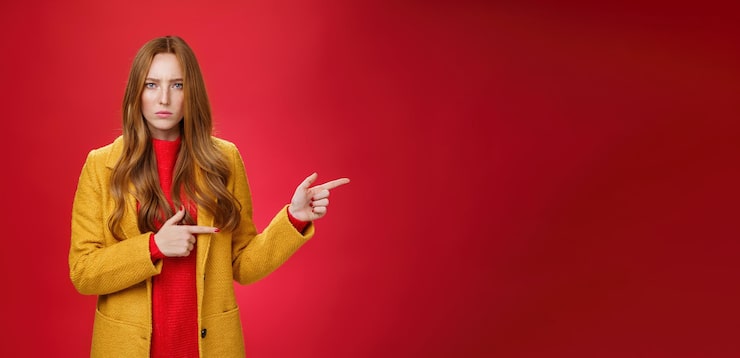 Ücretsiz Fotoğraf kızgın ve gücenmiş, hayal kırıklığına uğramış, sarı paltolu kızıl saçlı kadın, sert ve ciddi bir şekilde kaşlarını çatıyor