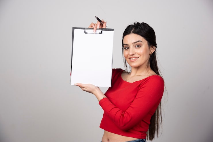 Ücretsiz Fotoğraf uzun saçlı gülümseyen kadın, kurşun kalemle bir not defteri gösteriyor.