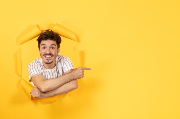 Ücretsiz Fotoğraf yırtık sarı kağıt yüzeyde gülümseyen genç adam