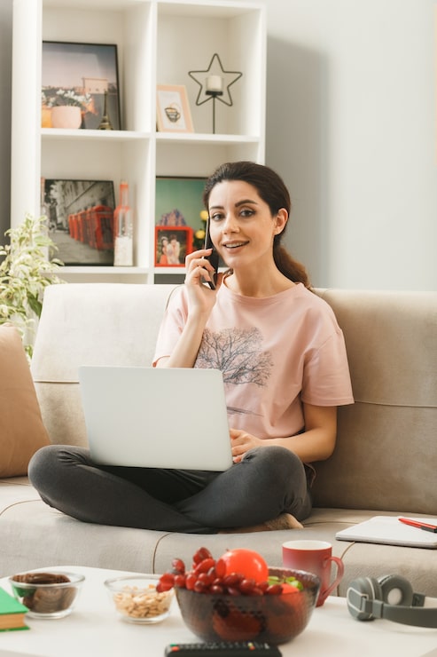 Gratis Foto jonge vrouw met laptop spreekt aan de telefoon zittend op de bank achter de salontafel in de woonkamer