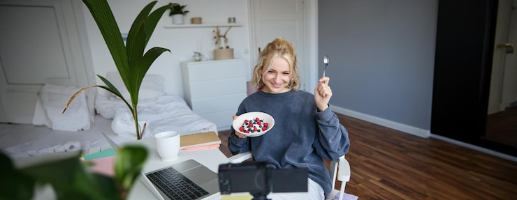 Gratis Foto portret van een schattig jong meisje vlogger die haar ontbijt toont op camera die vlog opneemt in haar slaapkamer
